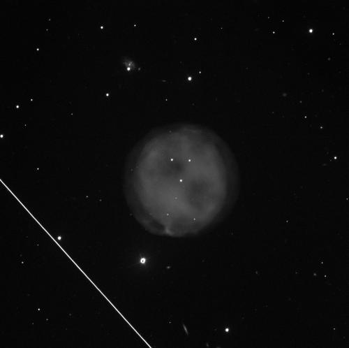 A dark grey, cloudy nebula in the middle against a black background with some small, white dots of stars. Towards the lower left, there is a diagonal white line that cuts through part of the image.