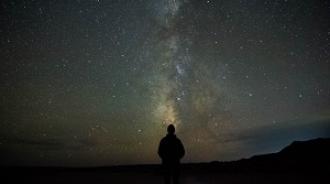 A silouette of a person standing in the dark with a night sky behind them showing lots of stars including the Milky Way