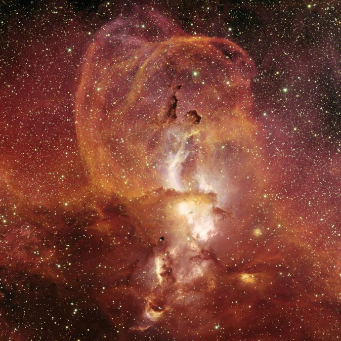 Clouds of reds and brown are dispersed throughout the image against a background of stars which can be seen as small, bright yellowish dots.